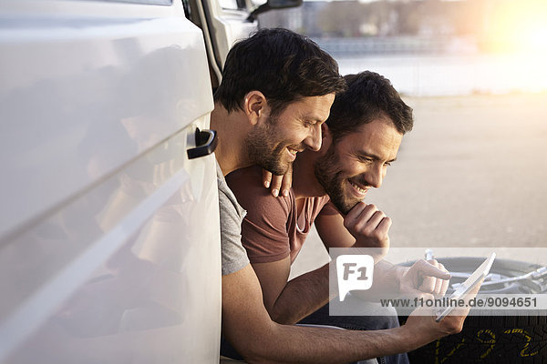 Zwei Männer sitzen im Auto und schauen auf ein digitales Tablett.