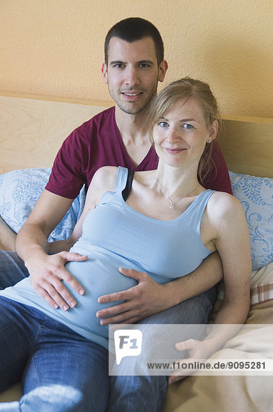 Couple expecting a baby sitting on bed at home