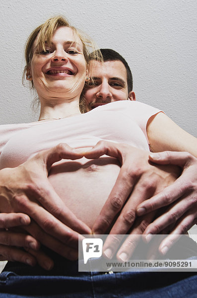 Glückliches Paar  das ein Baby erwartet  das mit den Fingern ein Herz formt.
