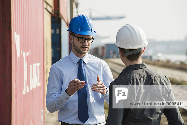 Businessman talking to teenager at container terminal