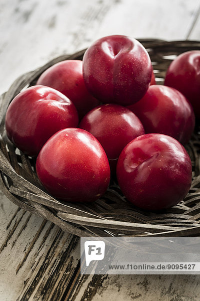 Bowl of red plums on wooden table