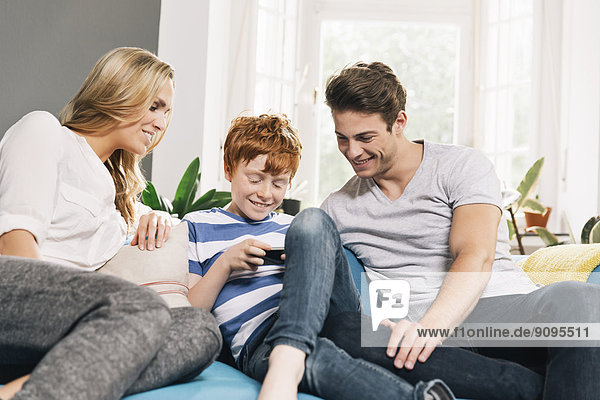 Junge Familie sitzt auf der Couch und schaut auf das Smartphone