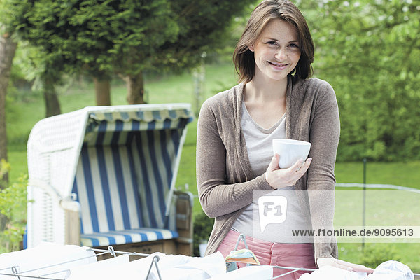 Porträt einer jungen lächelnden Frau mit einer Tasse Kaffee im Garten