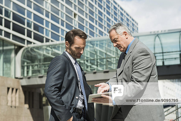 Two businessmen with digital tablet outside office building