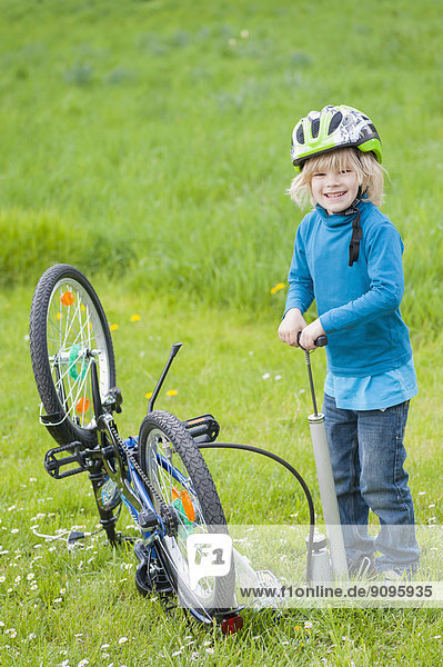 Little boy inflating bicycle tire on a meadow