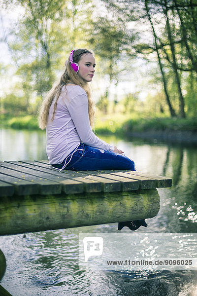Porträt einer Teenagerin mit rosa Kopfhörern auf Holzsteg