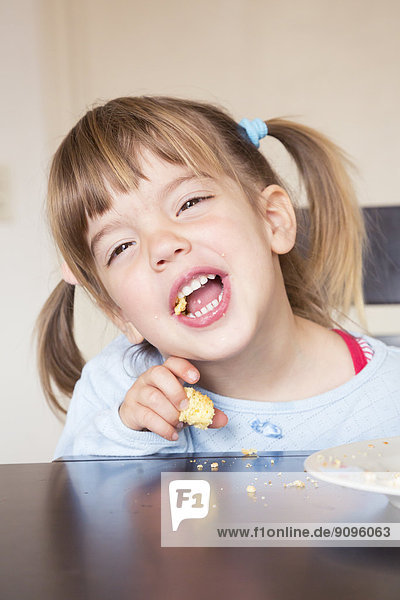 Porträt des kleinen Mädchens beim Kuchenessen mit offenem Mund