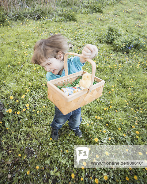 Fröhlicher kleiner Junge mit Korbtanz im Garten