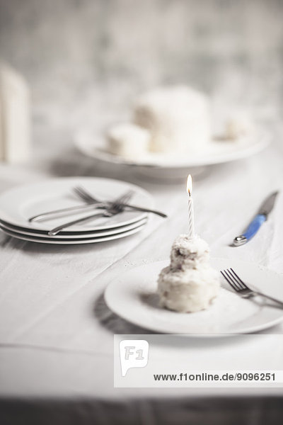 Mini-Kokosnuss-Geburtstagskuchen mit angezündeter Kerze auf dem Teller