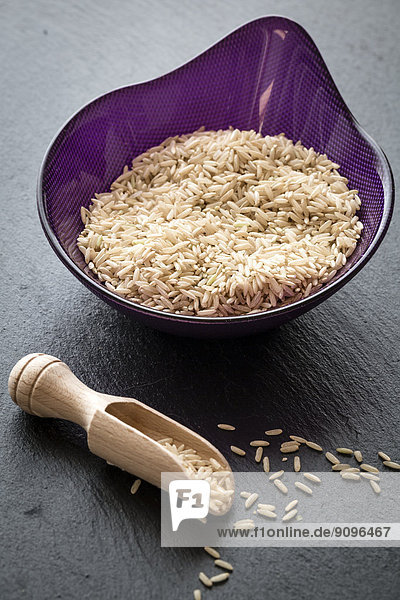 Bowl of organic brown rice and wooden shovel on slate