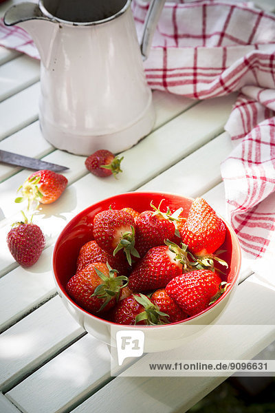 Schale mit Erdbeeren  Küchentuch und Glas auf weißem Holz
