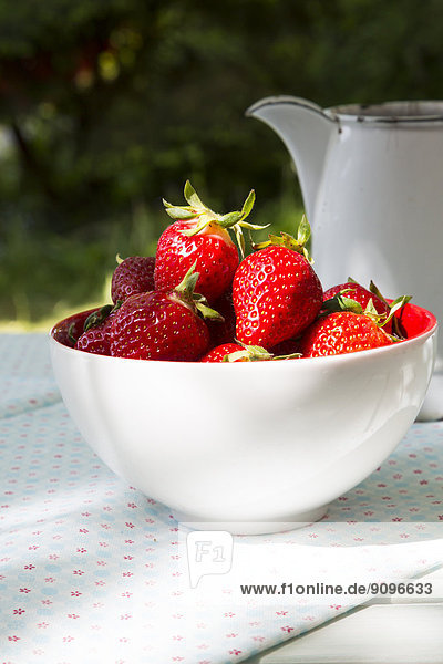 Schale mit Erdbeeren und Glas auf Tuch im Garten