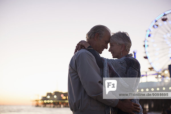 Seniorenpaar bei Sonnenuntergang am Strand umarmend
