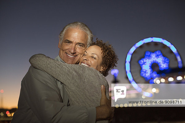 Porträt eines Paares  das sich nachts außerhalb des Vergnügungsparks umarmt.