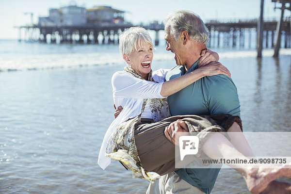 Senior man carrying wife on sunny beach