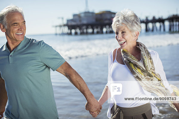 Enthusiastisches Seniorenpaar beim Laufen am Strand