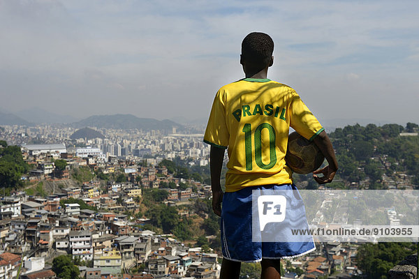 Boy  13 years  wearing the jersey of the Brazilian national team  holding a football  overlooking slums  favela  Rio de Janeiro  Brazil