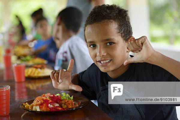 Brasilianischer Junge vor einem vollen Teller am Tisch mit anderen Kindern in einem Sozialprojekt für Straßenkinder  Maranguape  Ceará  Brasilien