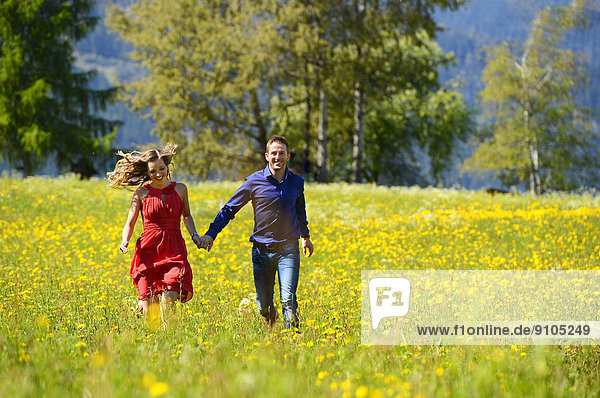 Glückliches Liebespaar läuft über eine Blumenwiese  im Frühling  Tirol  Österreich