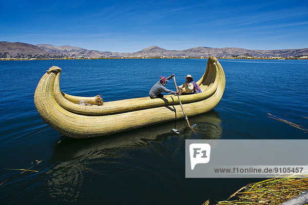 Zwei Einheimische rudern mit einem traditionellen Boot aus Totora-Schilf über den Titicacasee  Südperu  Peru