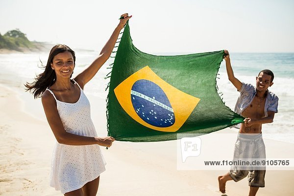 Young couple holding up Brazilian flag  Arpoador beach  Rio De Janeiro  Brazil