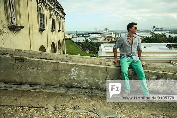 Young man sitting on wall next to Castillo San Felipe del Morro  Old San Juan  Puerto Rico