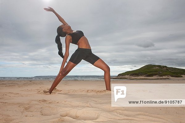 Young woman practicing yoga position on beach