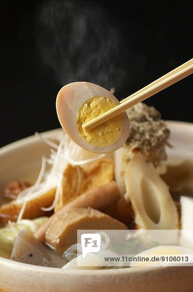 Chopstick picking up egg from bowl of noodles