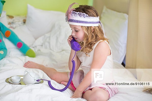 Young girl playing with toy telephone on bed