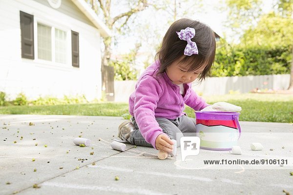 Female toddler playing with chalk on paving slabs