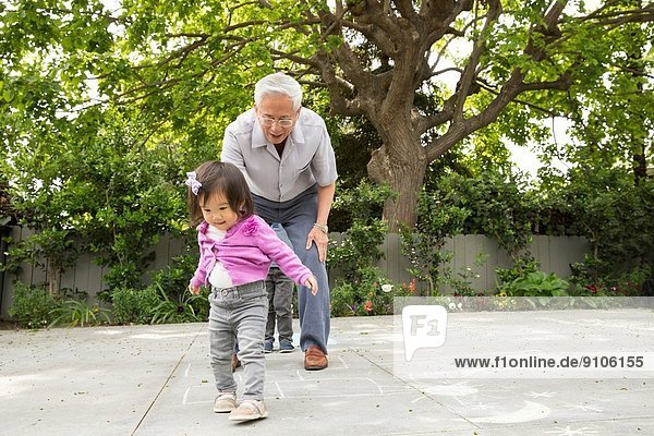 Grandfather playing hopscotch with toddler granddaughter