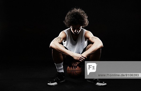 Basketballspieler sitzend auf Basketball