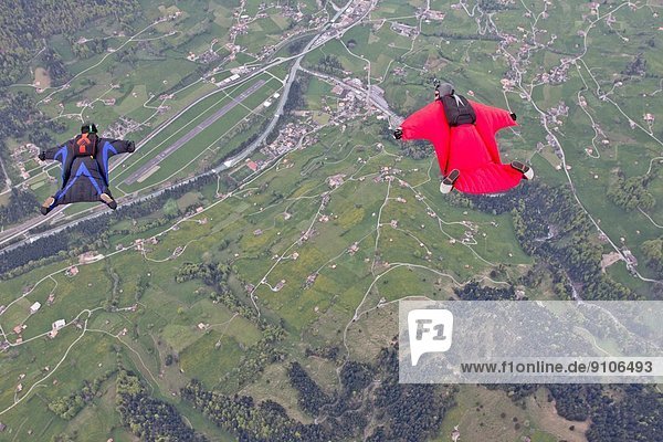 Zwei Männer  die in Wingsuits über Felder fliegen.
