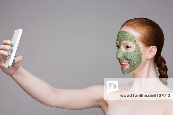 Junge Frau mit Gesichtsmaske  Selbstporträtfotografie mit Smartphone
