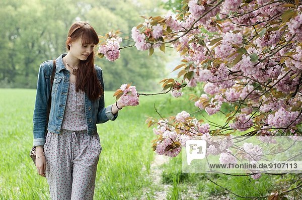 Junge Frau schlendert im Feld und berührt Blüten