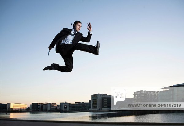 Mittlerer Erwachsener Geschäftsmann  der in der Luft springt  Kopenhagener Hafen  Dänemark