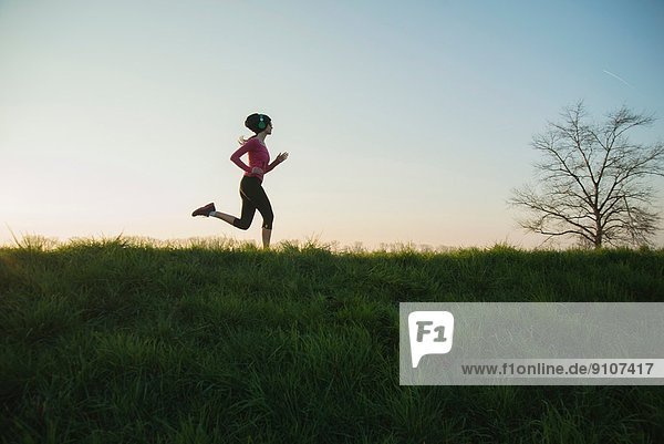 Junge Läuferin mit Silhouette auf dem Hügel