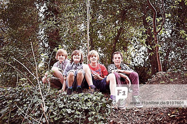 Porträt von vier Jungen im Wald sitzend