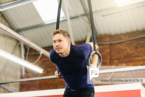 Man pulling suspended rings in gym