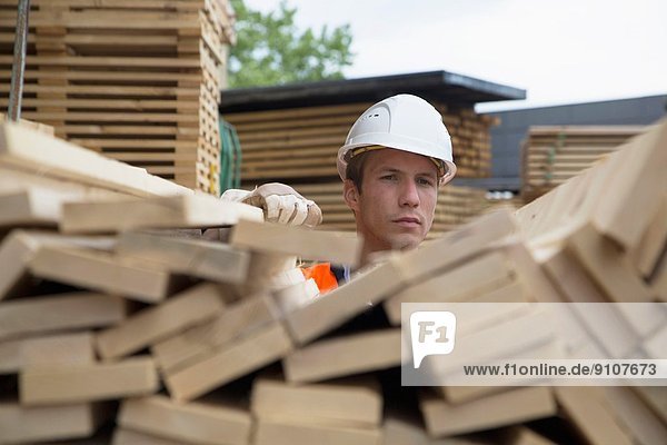 Porträt eines jungen Mannes hinter Holzbrettern im Holzplatz