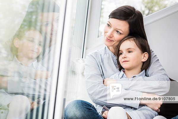 Mutter und Tochter umarmen sich am Fenster
