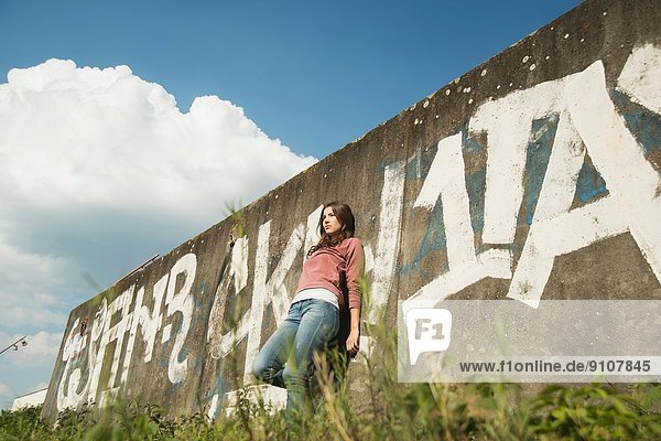 Young woman leaning against wall with graffiti