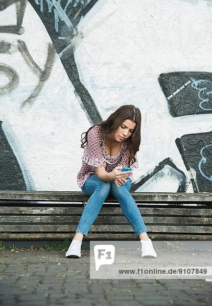 Young woman sitting on bench using cell phone