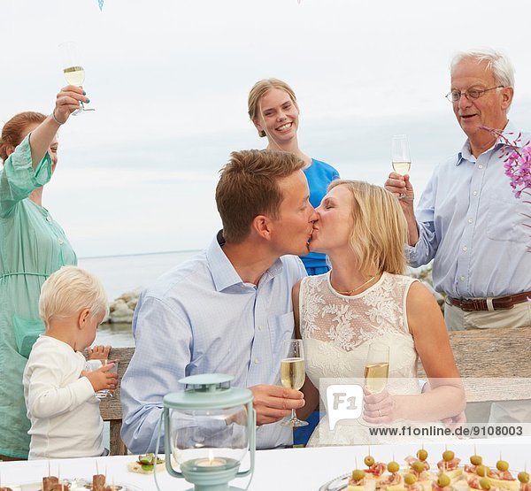 Mid adult couple kissing and making a toast with group of friends