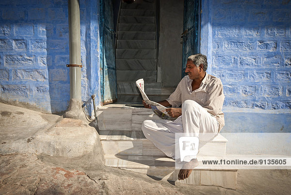 A man reads a newspaper on his doorstep in the streets of Jodhpur  Rajasthan State  India