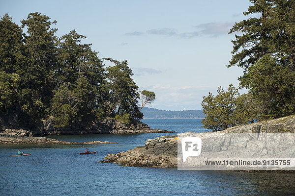 Two kayakers paddle through channel  Portland Island  Gulf Islands National Park  British Columbia  Canada