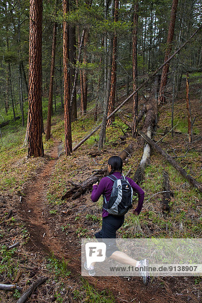 A young asian woman trail running in the 3 Blind Mice trail system. Penticton  BC