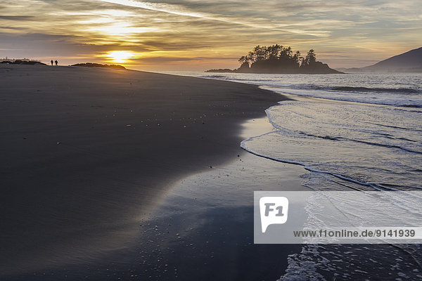 Waves wash the shoreline of Whaler Islet as the sun sets on Flores Island Provincial Park in the background.Clayoquot Sound  British Columbia Canada.