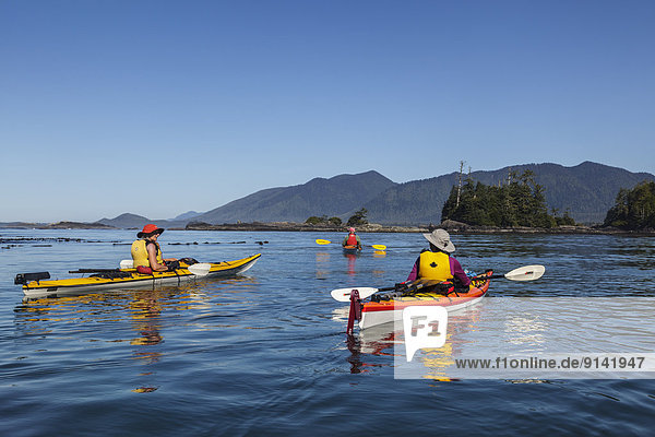 Three kayakers drift in the calm waters of Clayoquot Sound off the west coast of Vancouver Island British Columbia  Canada.Model Released