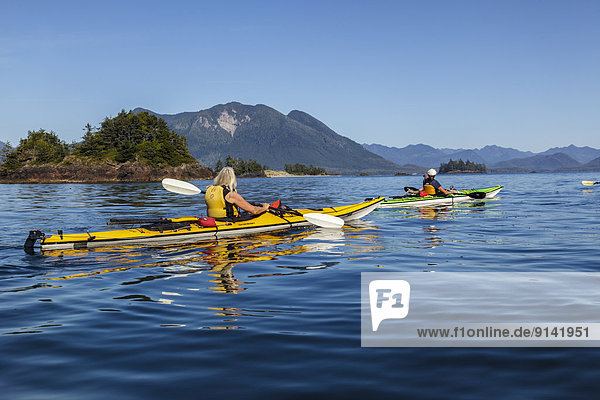 Two kayakers approach Whalers Islet in Clayoquot Sound off the west coast of Vancouver Island  British Columbia  Canada. Model Released